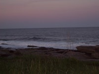 a man riding a surfboard on a rocky beach at dusk